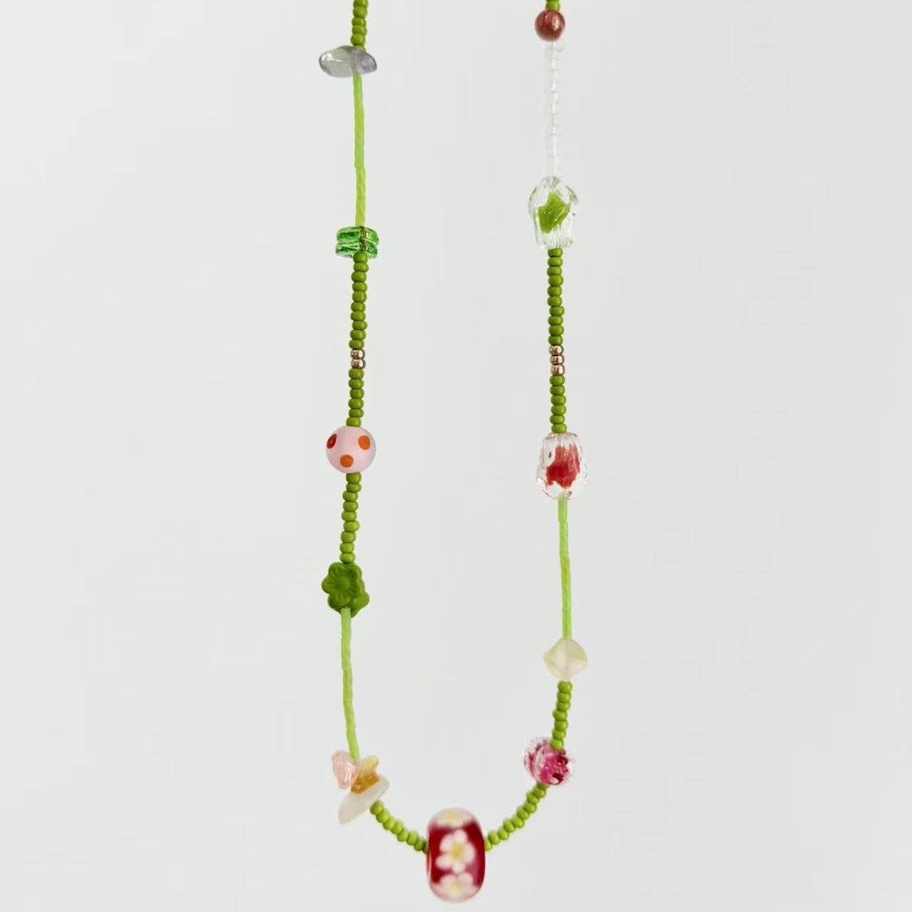 Necklace with green beads and colorful accents on a light gray background