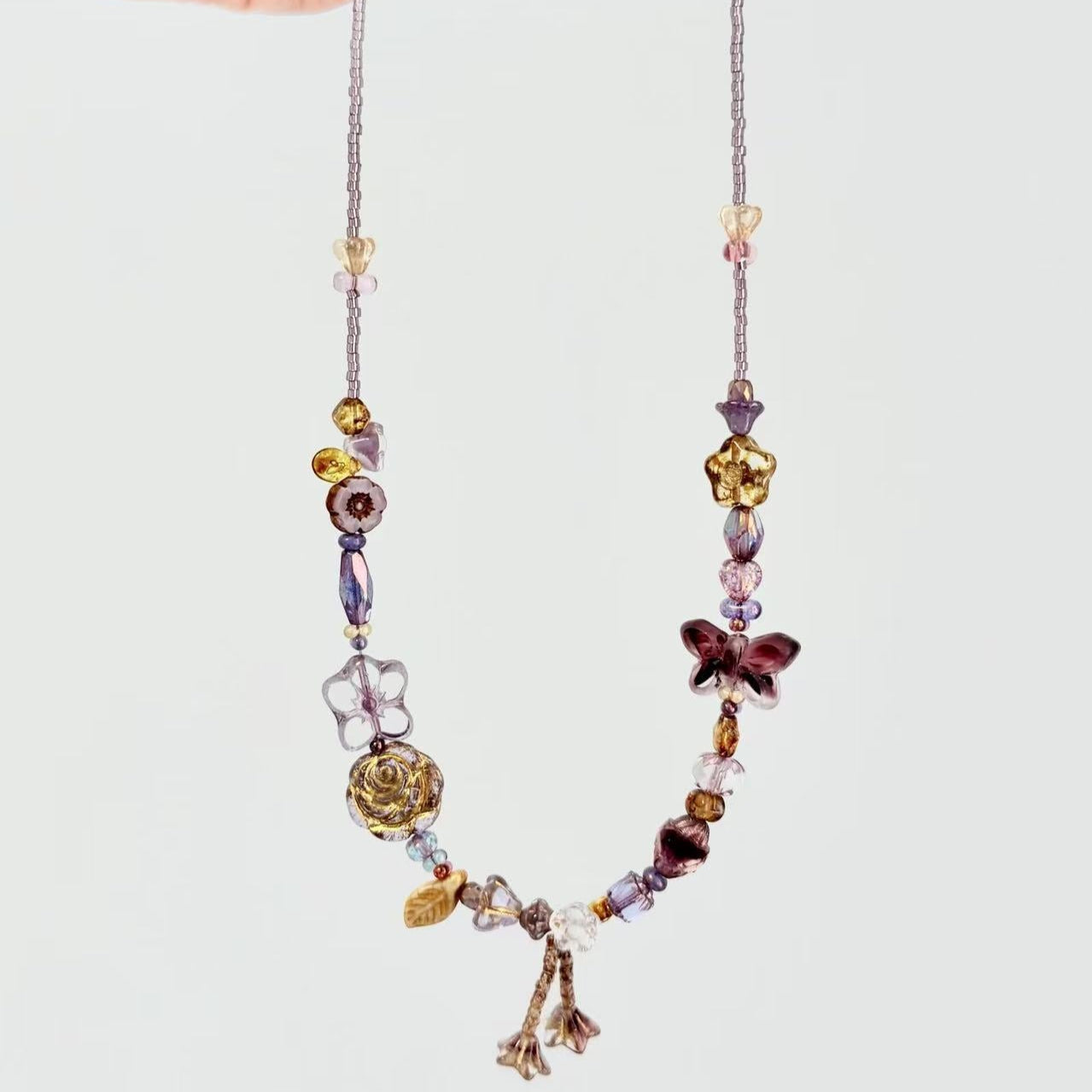 Colorful beaded necklace with charms held by a hand on a light gray background