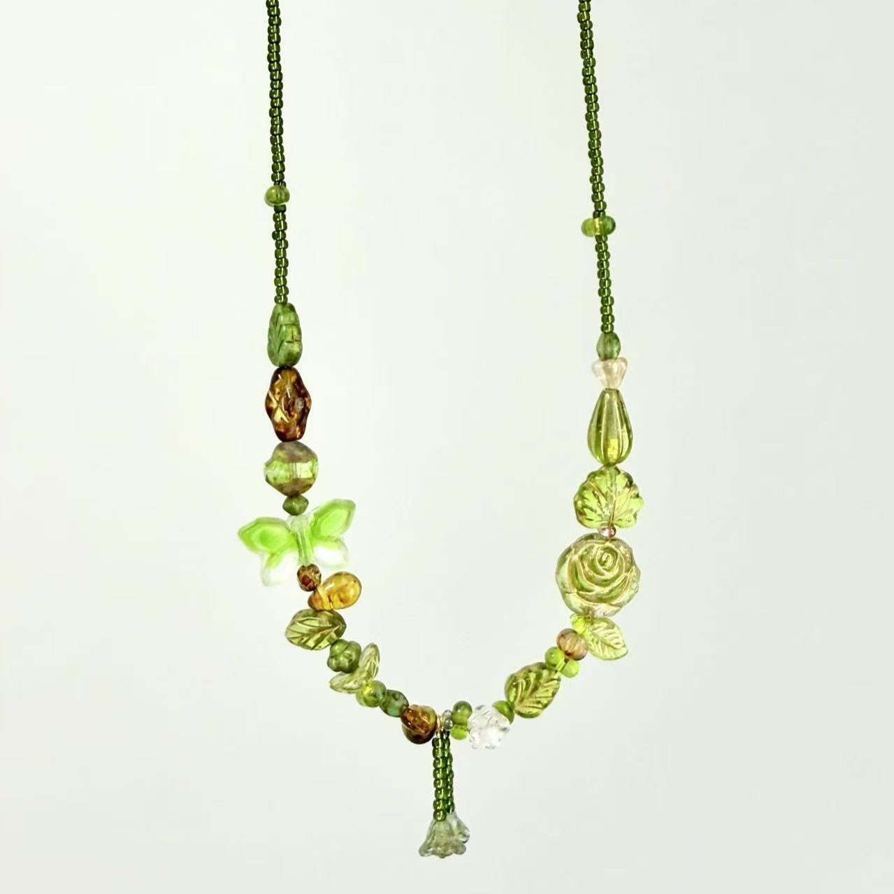 Green beaded necklace with floral and butterfly designs on a white background